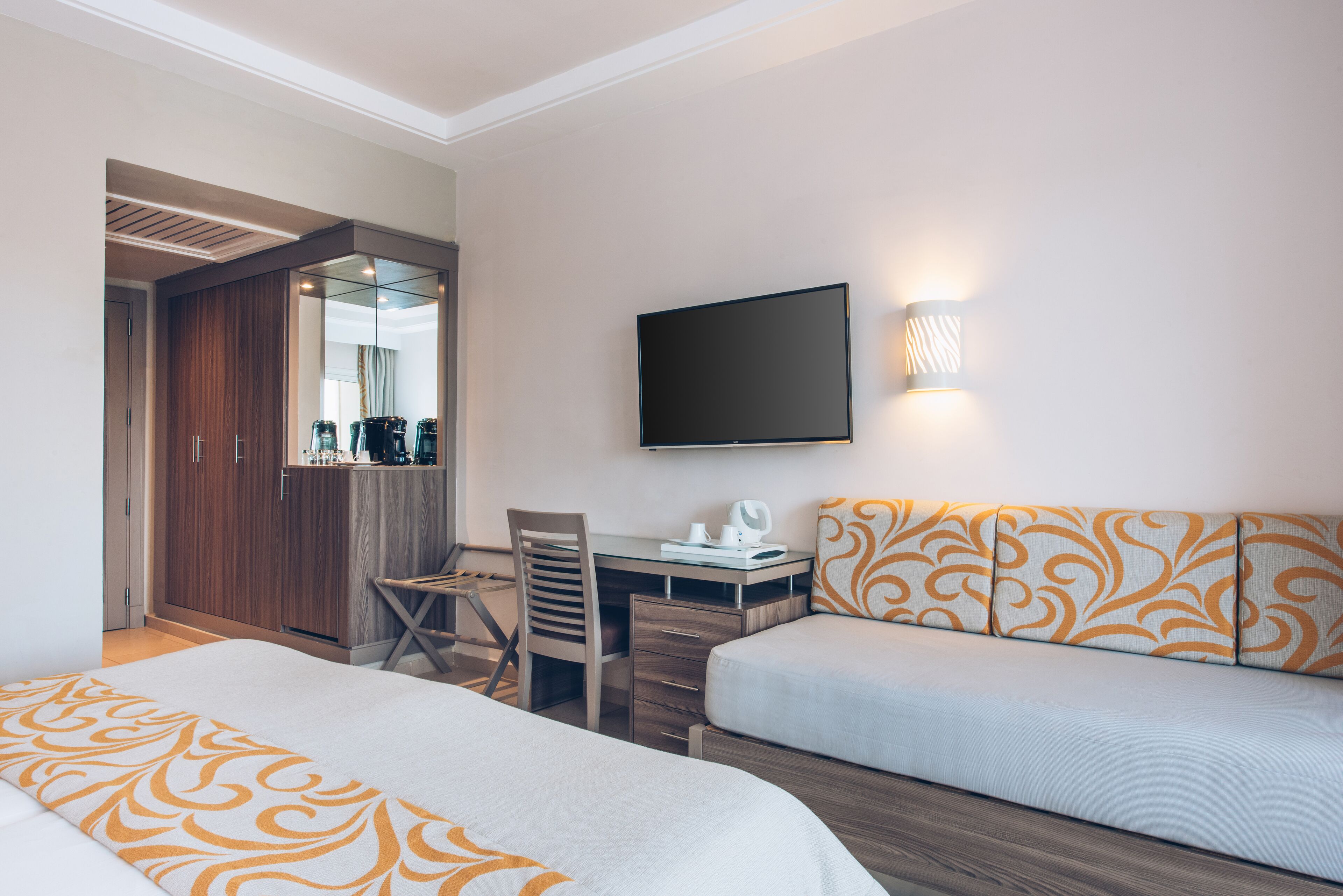 Habitación de hotel con dos camas, un escritorio con silla, un televisor y un espejo.