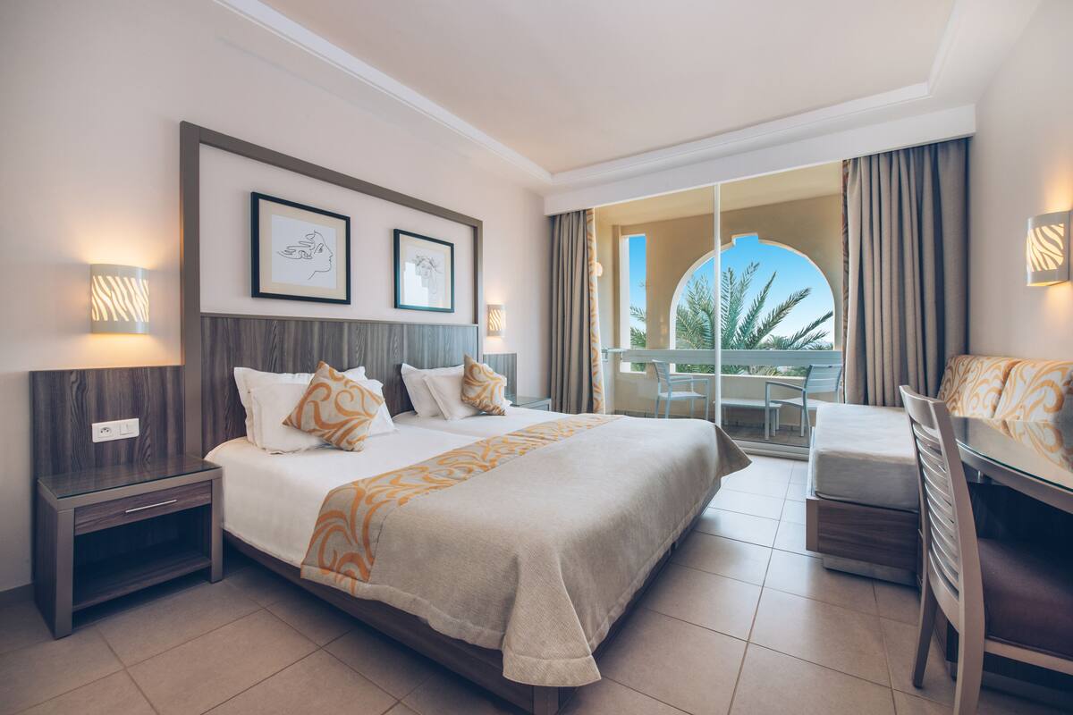 A hotel room with a large bed, a desk, and a balcony with a view.