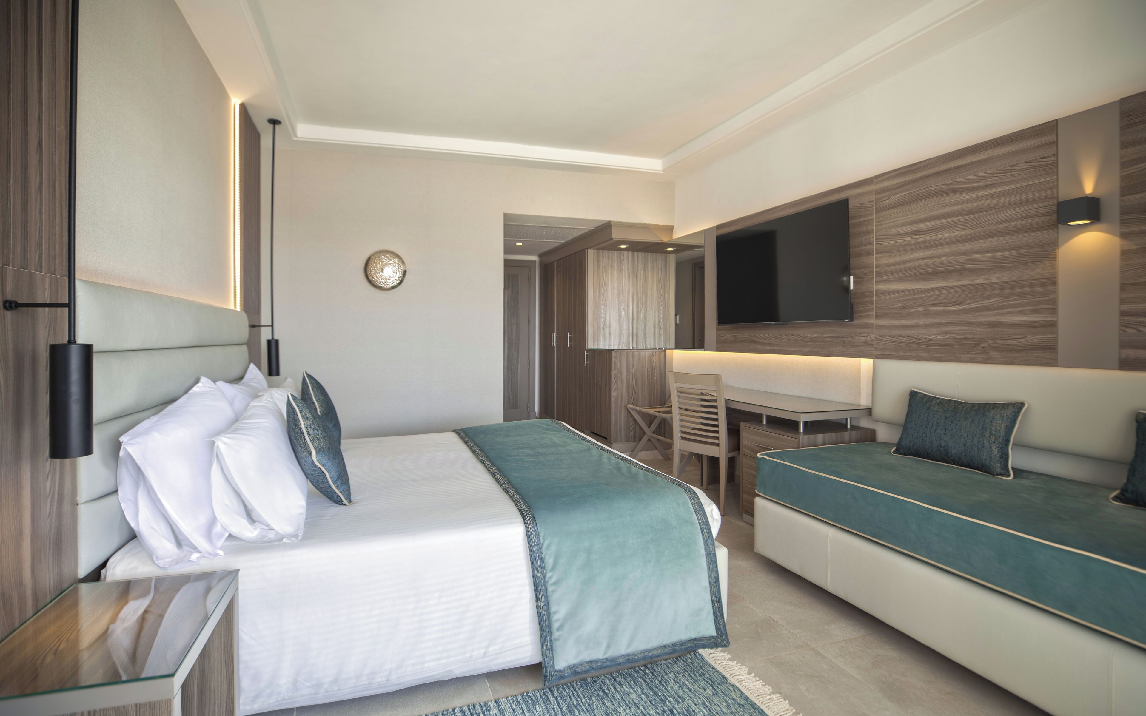 Ein modernes Hotelzimmer mit Bett, Sofa, Schreibtisch und Fernseher.