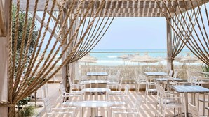 An outdoor seating area with tables and chairs, overlooking a beach with umbrellas. - Iberostar Waves Mehari Djerba (Djerba Midun)