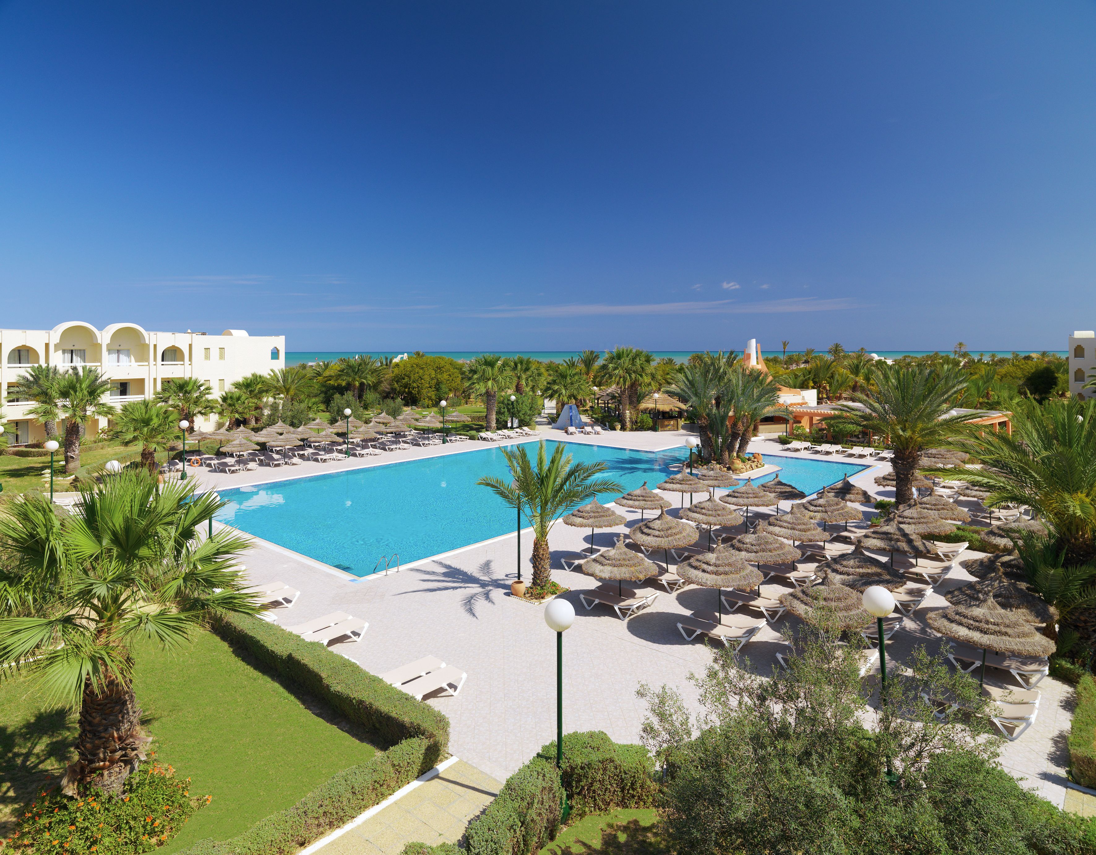 Un resort con una piscina grande, tumbonas y palmeras.
