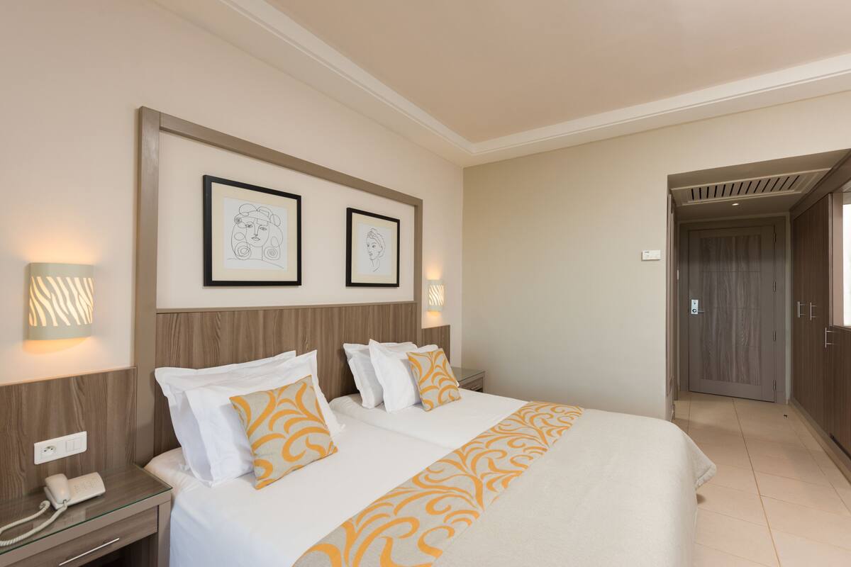 A hotel room with two beds, a bedside table with a phone, and framed artwork on the wall.