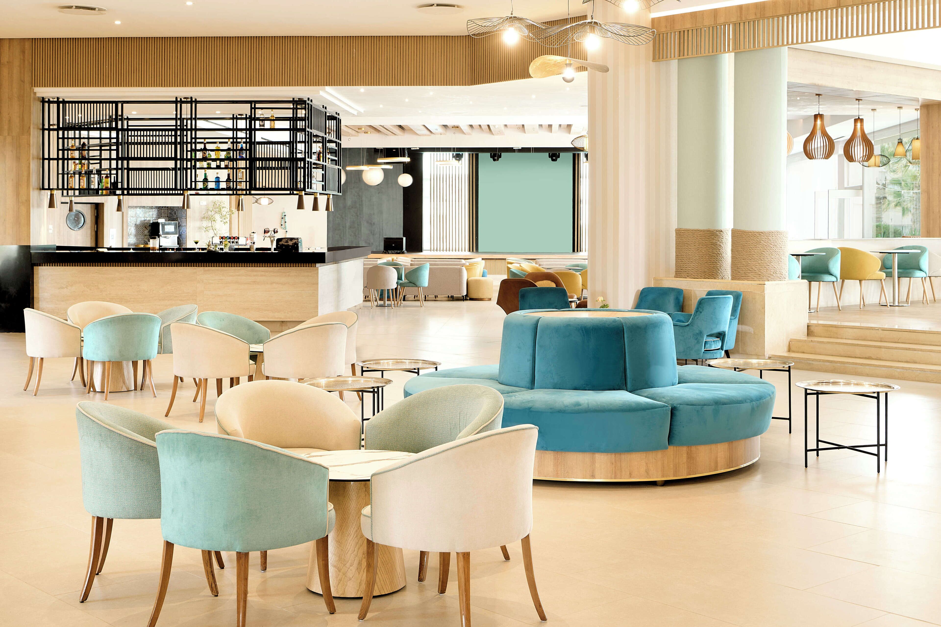 A modern lounge area with seating arrangements, a bar, and a large window providing natural light.