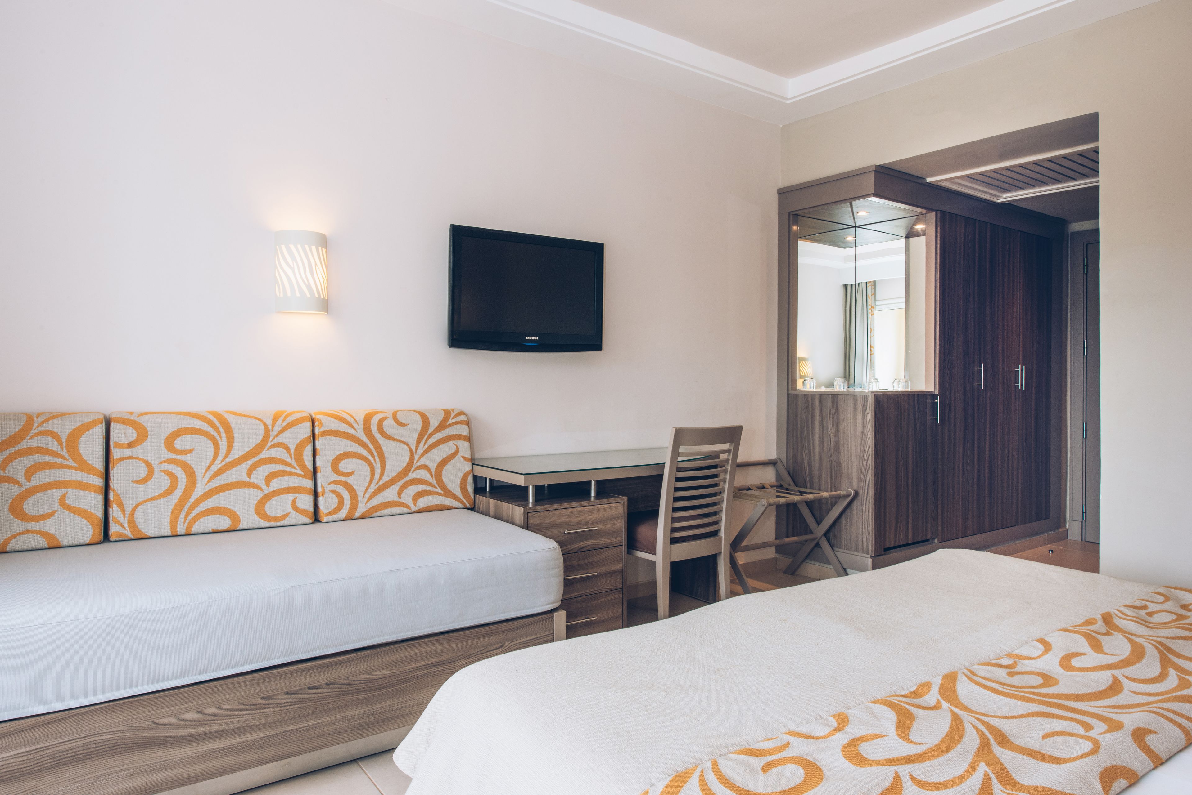 Una habitación de hotel con cama, escritorio, silla, televisor y armario.
