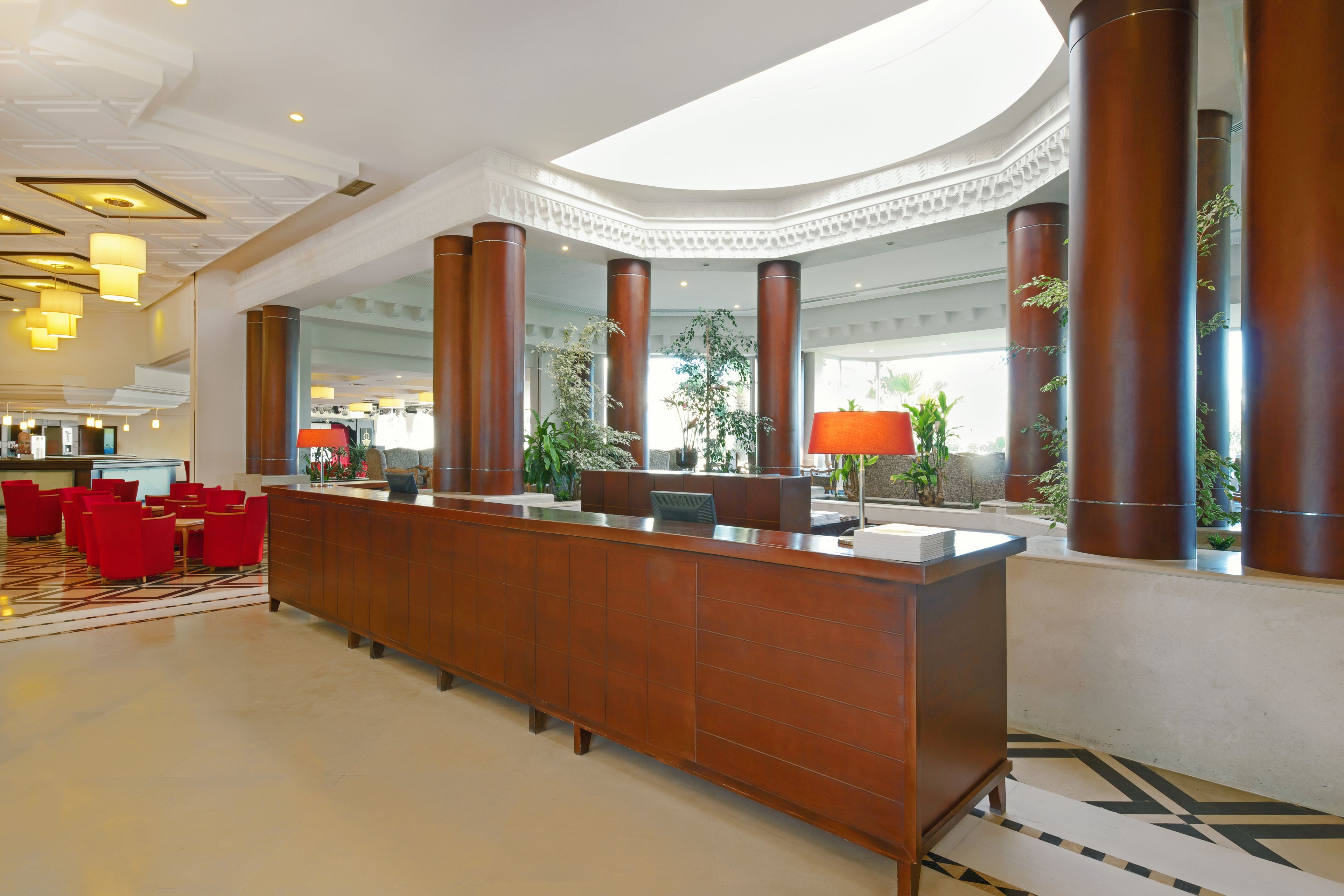 Eine Hotelhalle mit einer Rezeption, roten Stühlen und großen Fenstern.