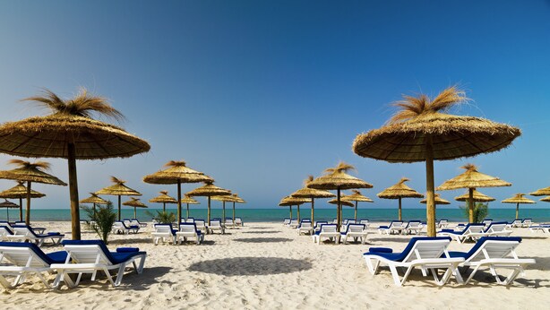 A beach with rows of white lounge chairs and thatched umbrellas. - Iberostar Waves Mehari Djerba (Djerba Midun)