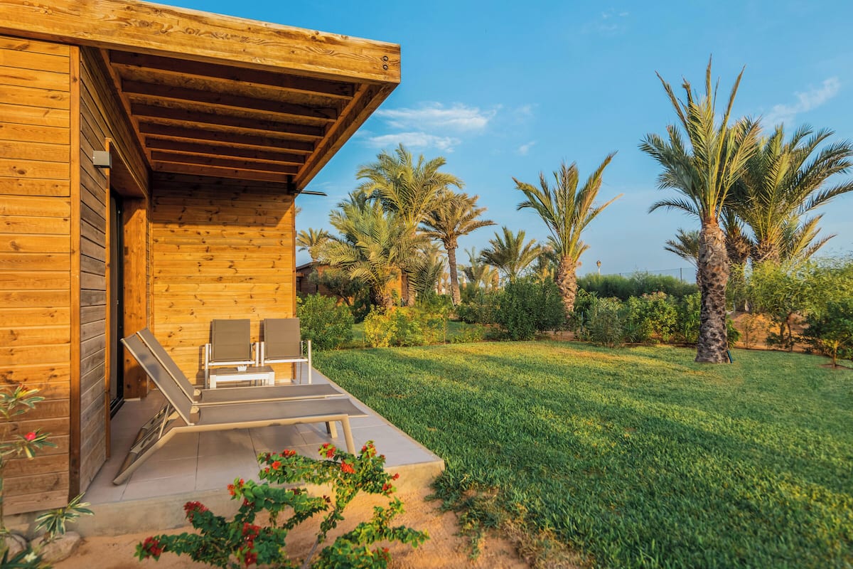 A wooden building with a covered outdoor seating area and a well-maintained garden with palm trees.