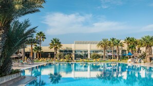 A swimming pool with lounge chairs and palm trees, surrounded by a modern building with large windows. - Iberostar Waves Mehari Djerba (Djerba Midun)