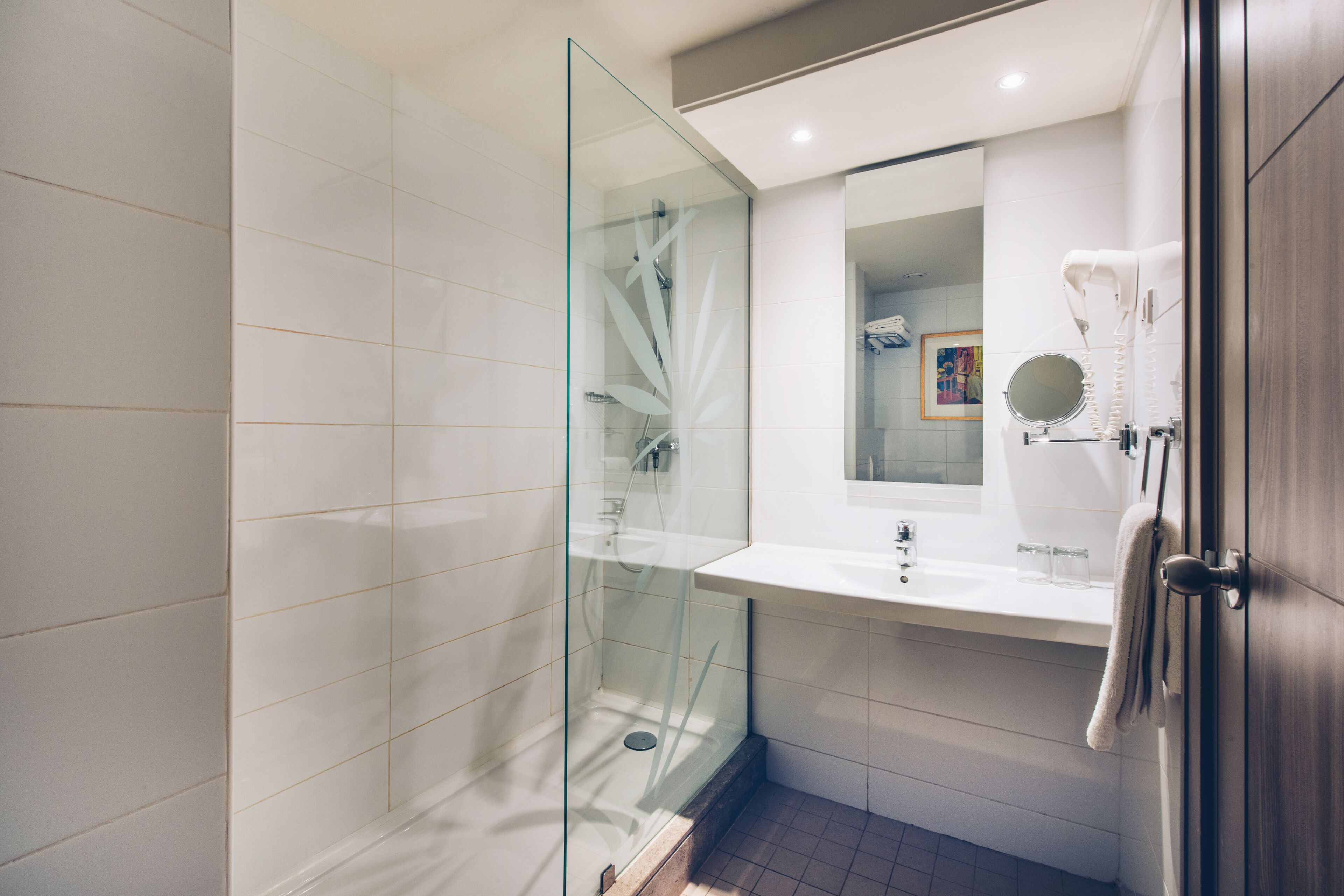 Un baño moderno con ducha de vidrio, lavamanos blanco y un secador de pelo fijado a la pared.