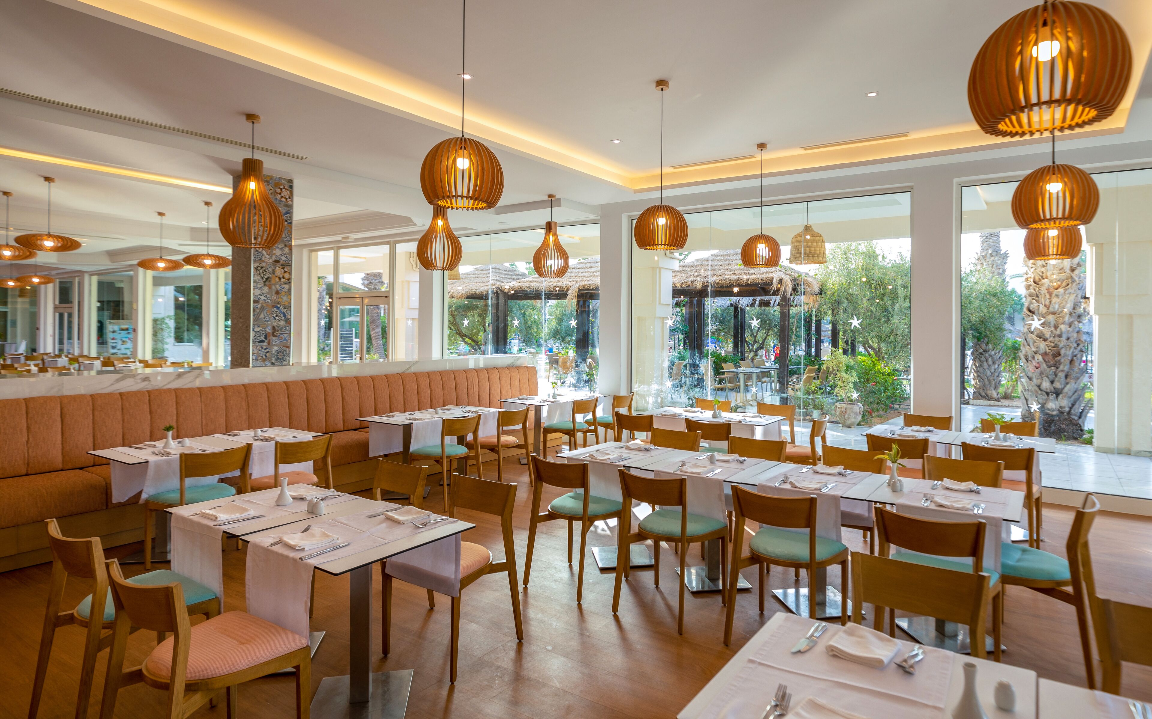 A restaurant with multiple tables and chairs, large windows, and hanging pendant lights.