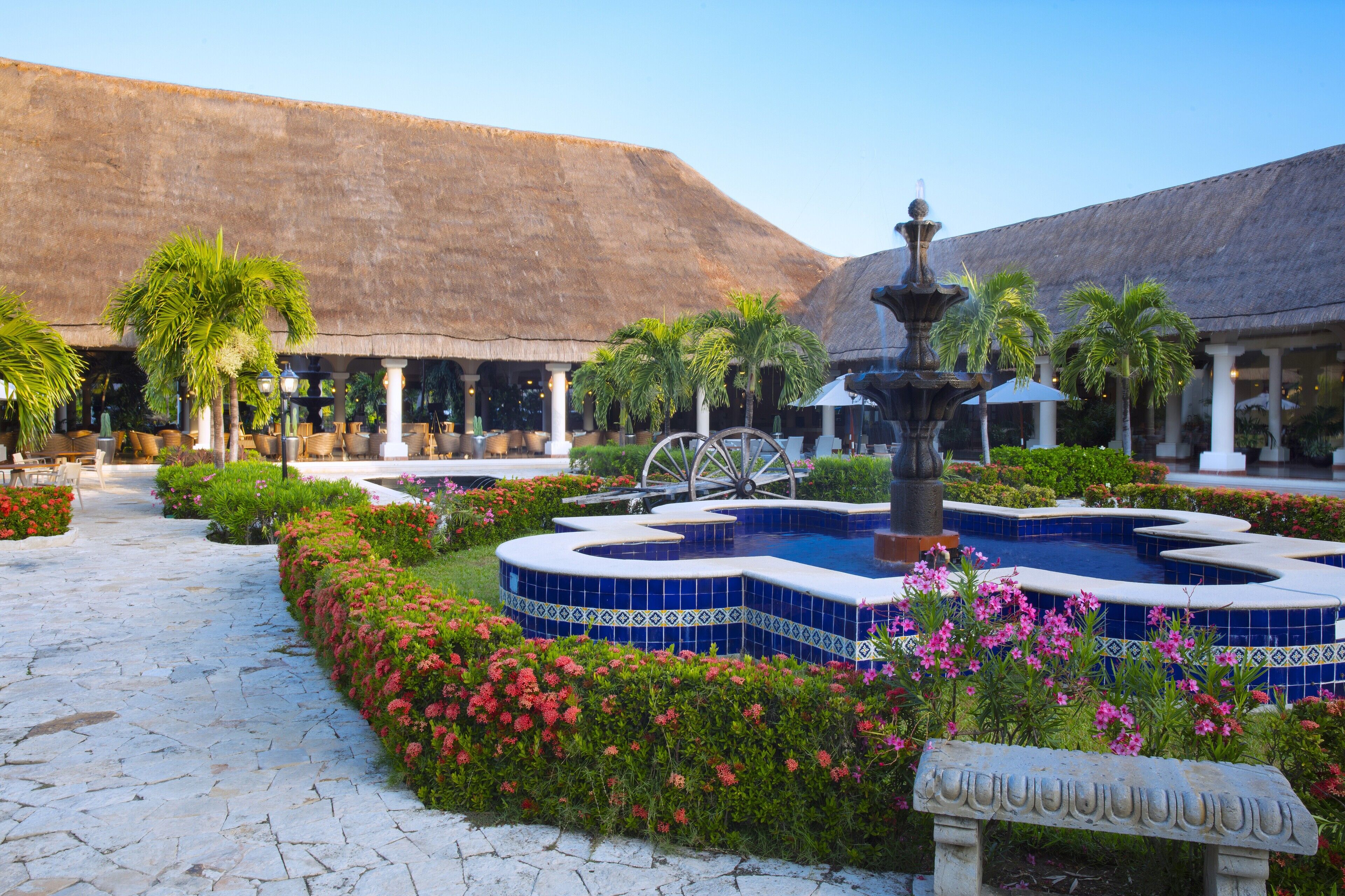 Un patio con una fuente, palmeras y un edificio con techo de paja.