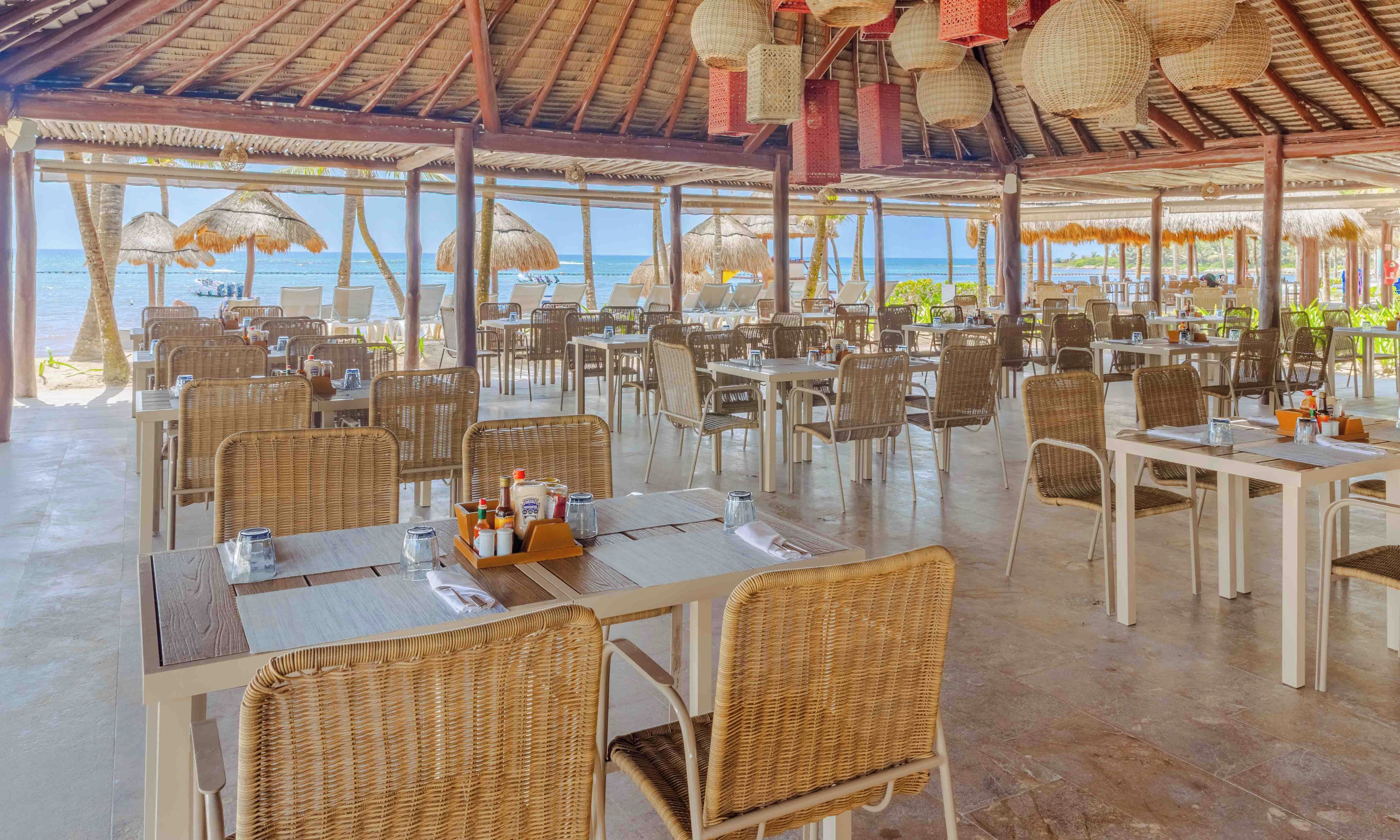 An outdoor dining area with wicker furniture, tables, and chairs, overlooking the sea.