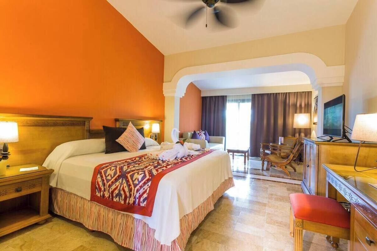A hotel room with a large bed, a desk, a chair, a television, and a ceiling fan.