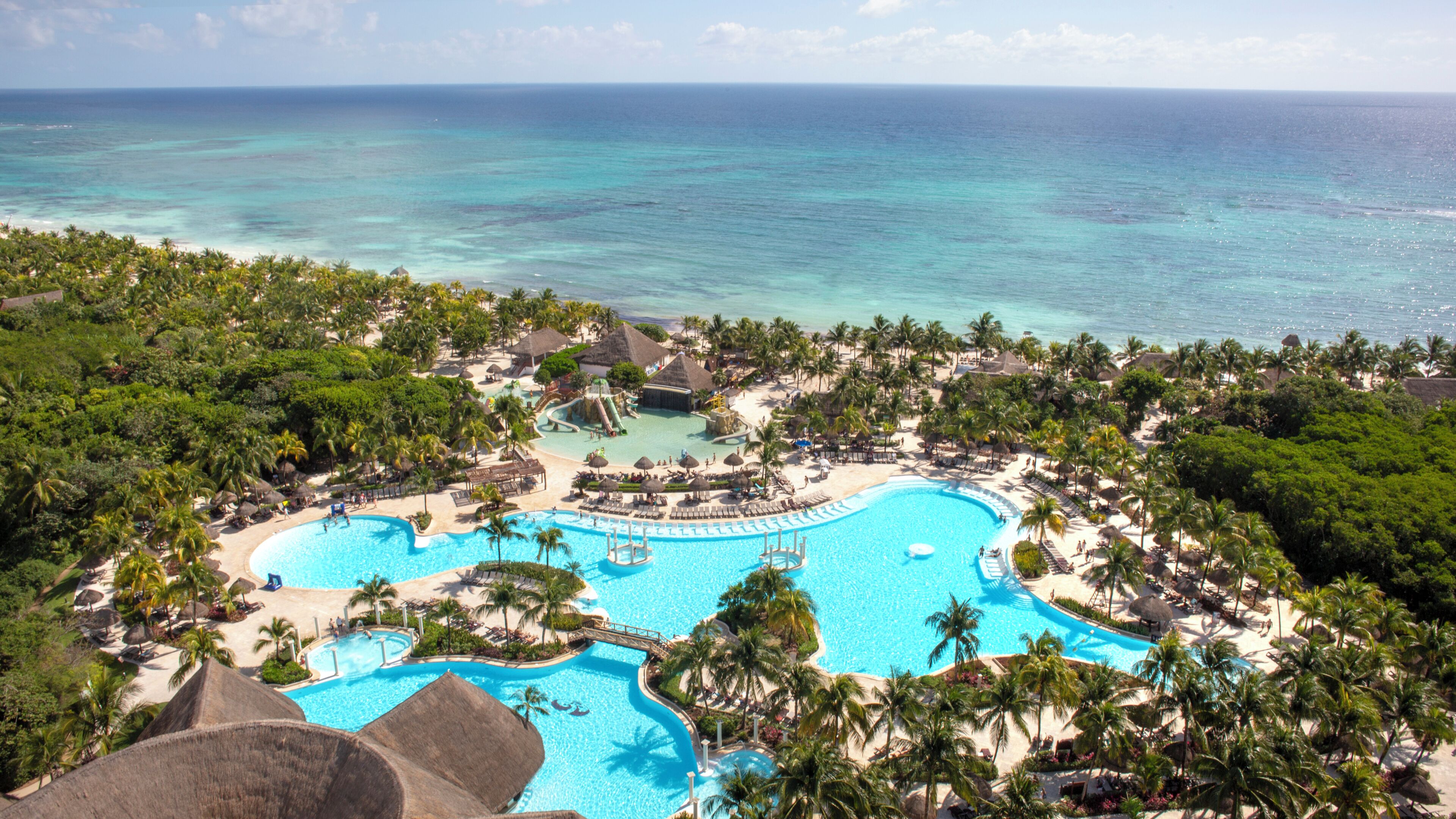 A resort with a large central pool, palm trees, and a beach.