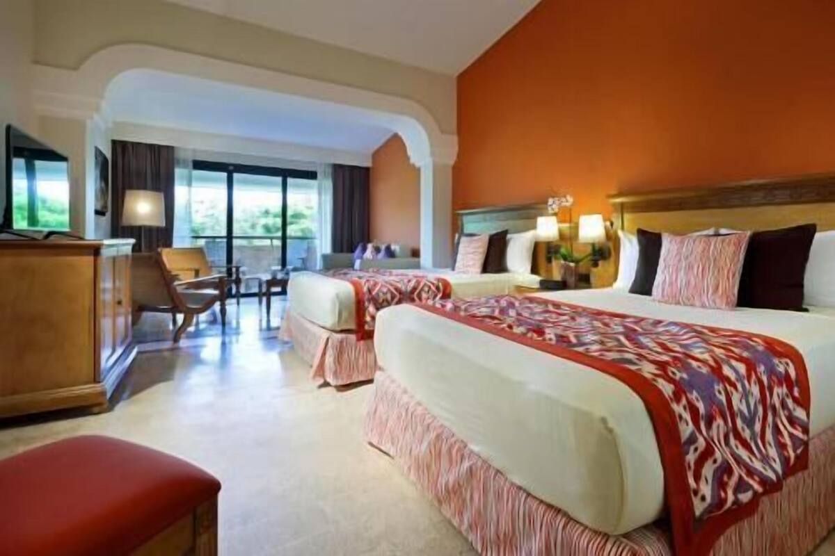 A hotel room with two beds, a desk, a chair, and a view of the outdoors.