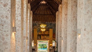 A corridor with stone columns, a wooden ceiling, and a view of an outdoor pool area. - Grand Palladium Colonial Resort & Spa All Inclusive (Kantenah)
