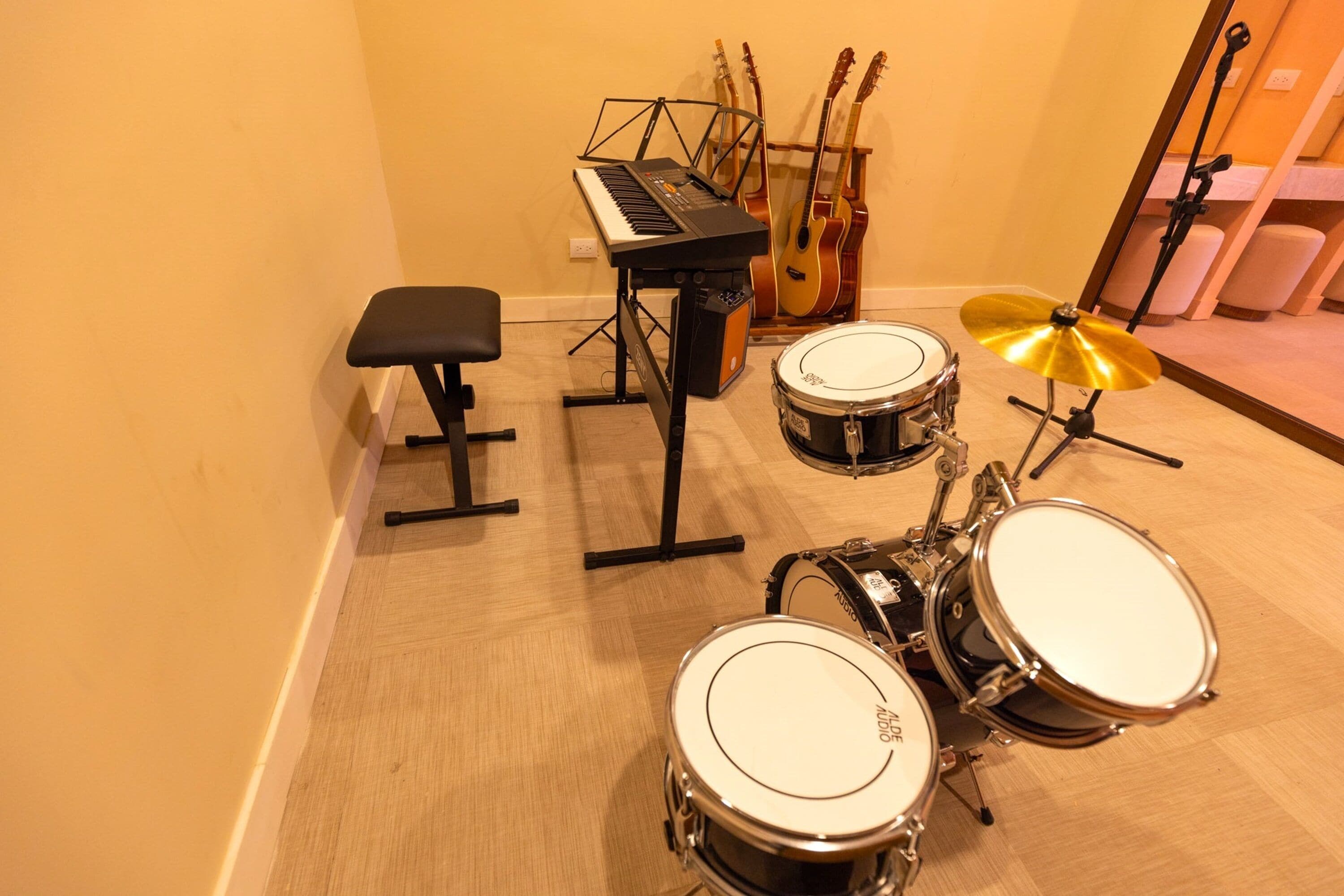 Une batterie avec un clavier et un tabouret, dans une pièce au plancher en bois et aux murs jaunes.