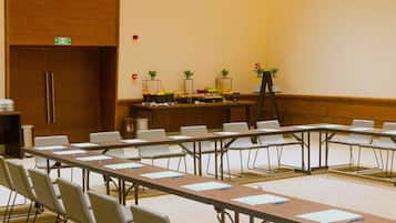 A conference room with long tables, chairs, and a buffet table with fruits and vegetables.