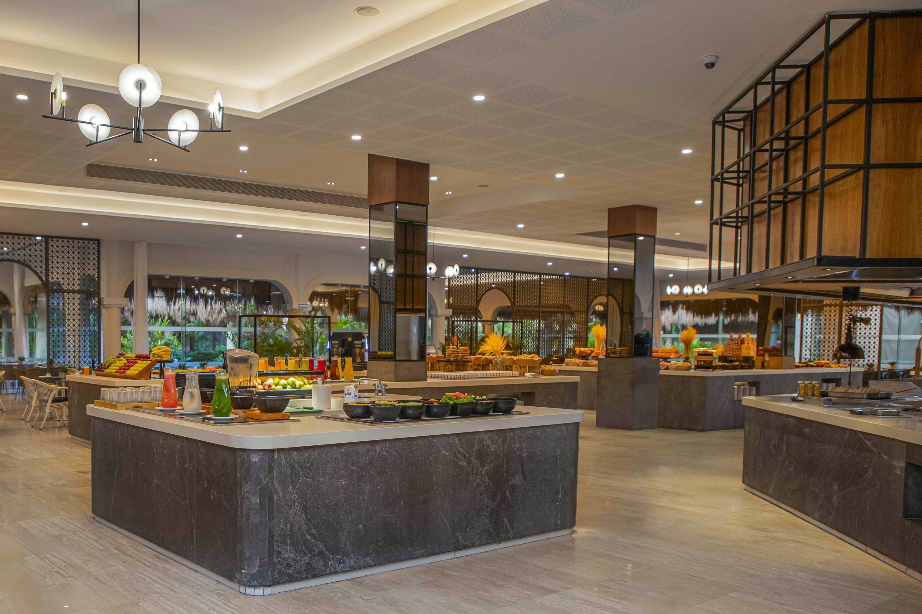 A spacious hotel lobby with a central island counter, multiple seating areas, and a modern ceiling design.