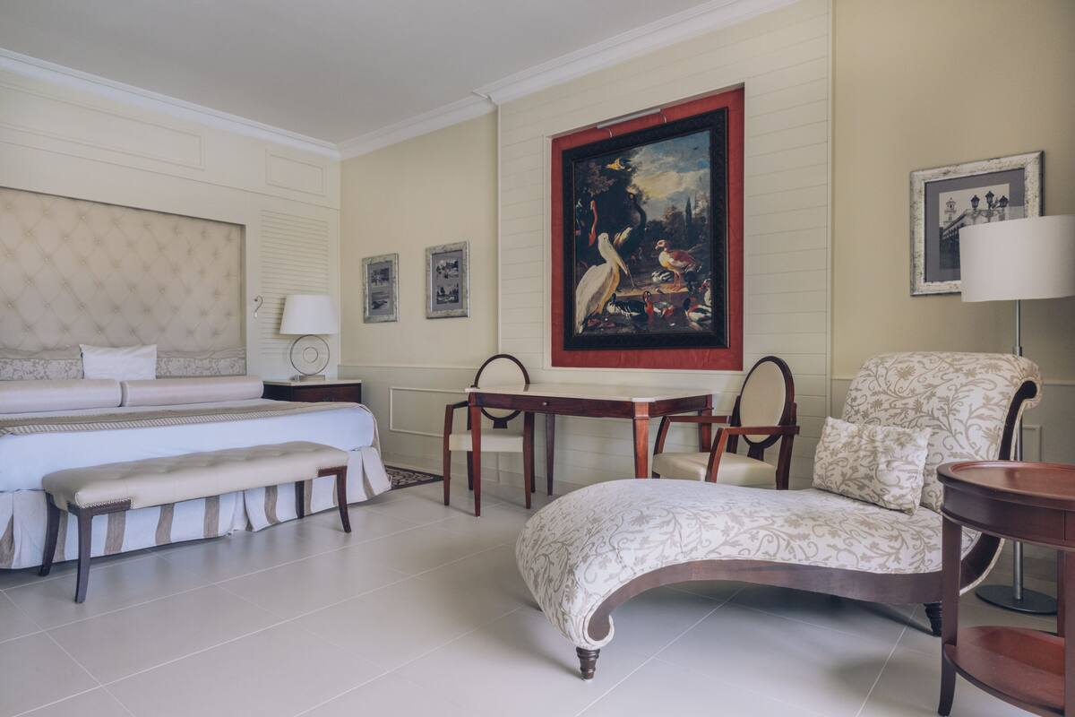 Ein Hotelzimmer mit Bett, einer Bank, einem Tisch, einem Stuhl und einem Bild an der Wand.
