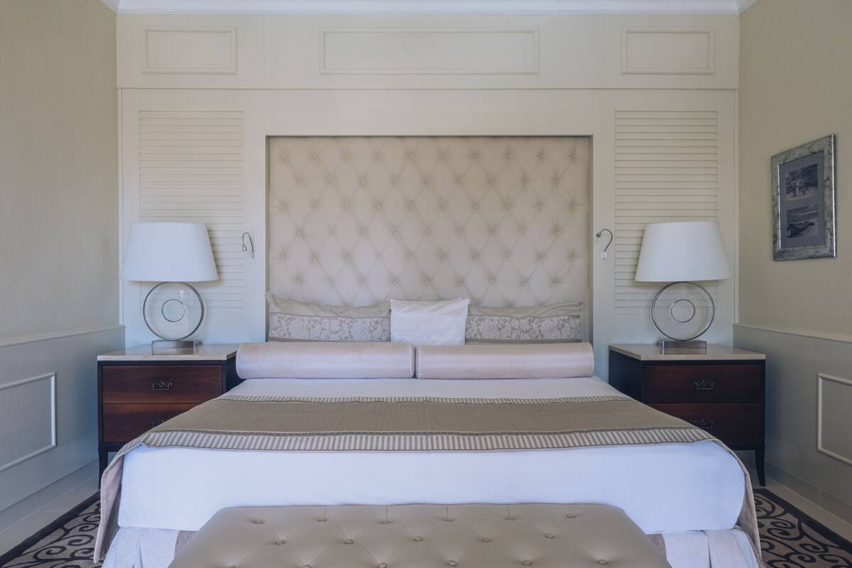 Ein ordentlich bezogenes Bett mit einer gebügelten Kopfstütze, zwei Nachttische mit Lampen und einem gemusterten Teppich.
