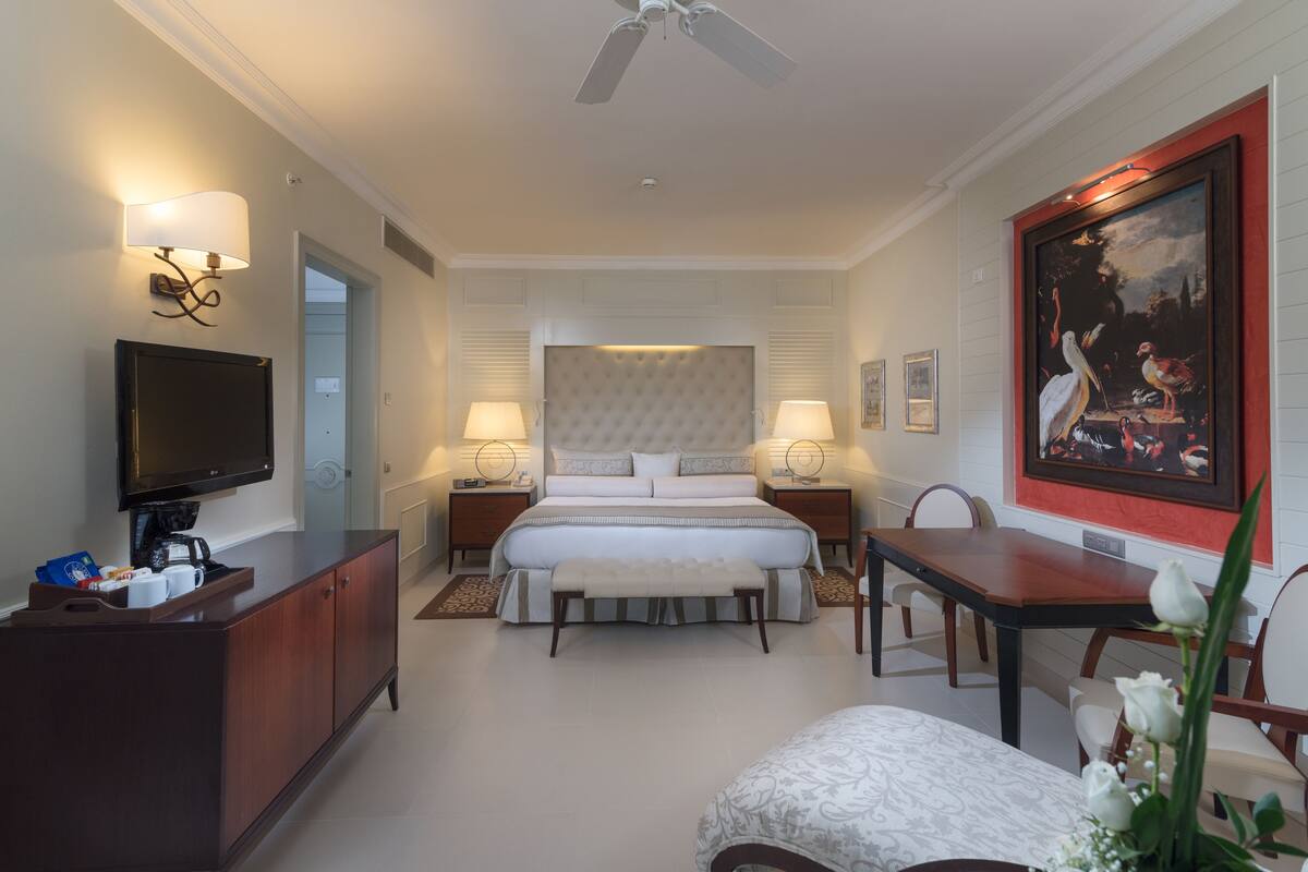 Ein Hotelzimmer mit einem großen Bett, Nachttischlampen, einem Fernseher, einem Schreibtisch und einem Esstisch.