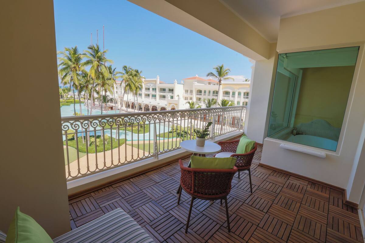 Ein Balkon mit Blick auf einen Pool und Palmen, ausgestattet mit Korbstühlen und einem kleinen Tisch.