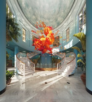 Un hall d’entrée spacieux, agrémenté d’un grand escalier, d’une fontaine et de grands pots de plantes.