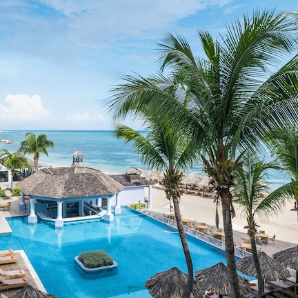 A resort pool area with lounge chairs, a bar, and a view of the ocean.