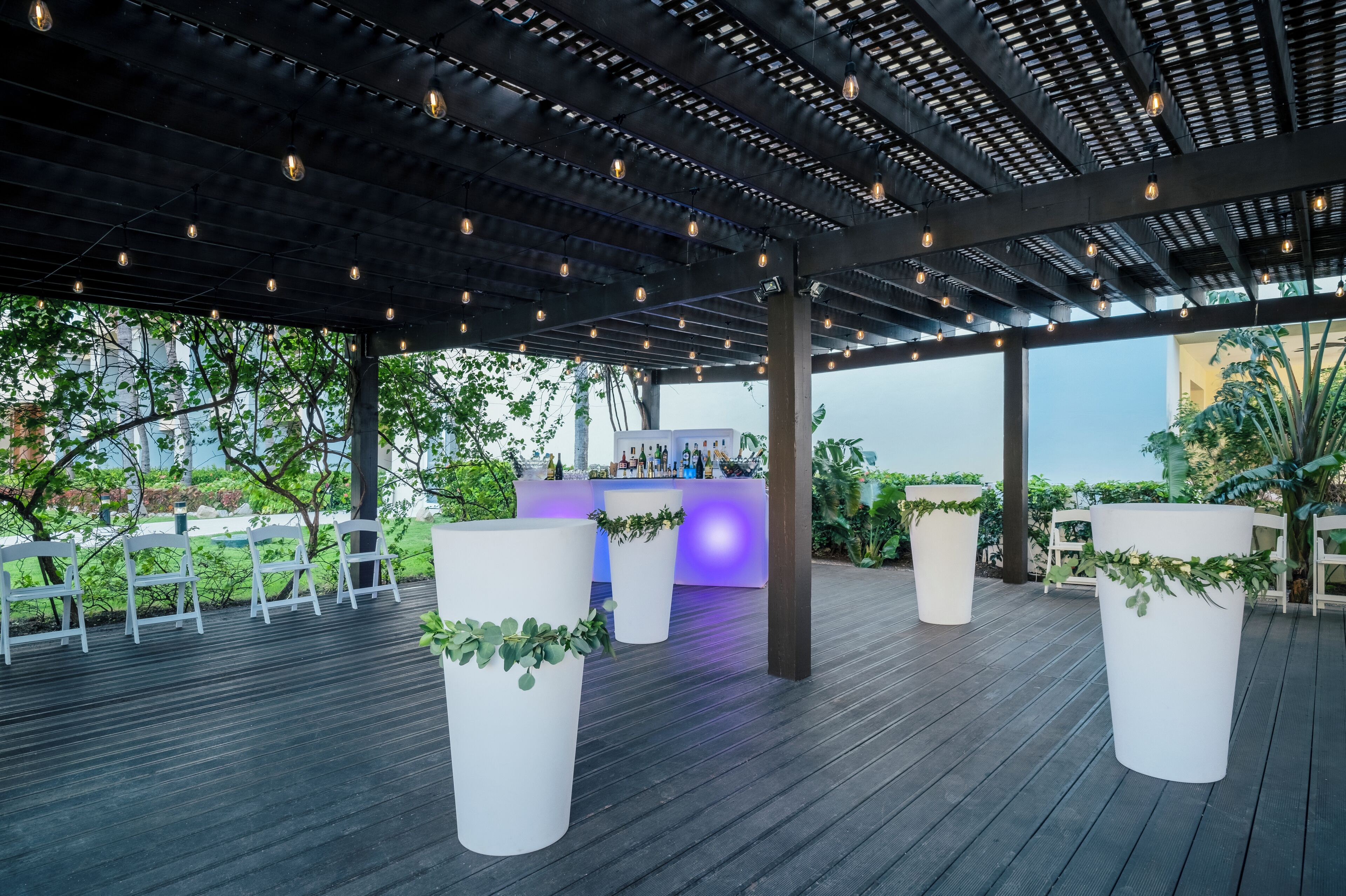 Un patio al aire libre con barra, sillas blancas y macetas.