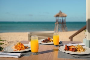 A beachside table with plates of food and two glasses of orange juice, overlooking the ocean. - JOIA Rose Hall by Iberostar - Adults Only - All Inclusive (Montego Bay)