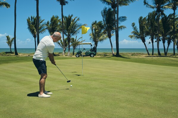 A golf course with a clear view of the ocean and palm trees in the background.