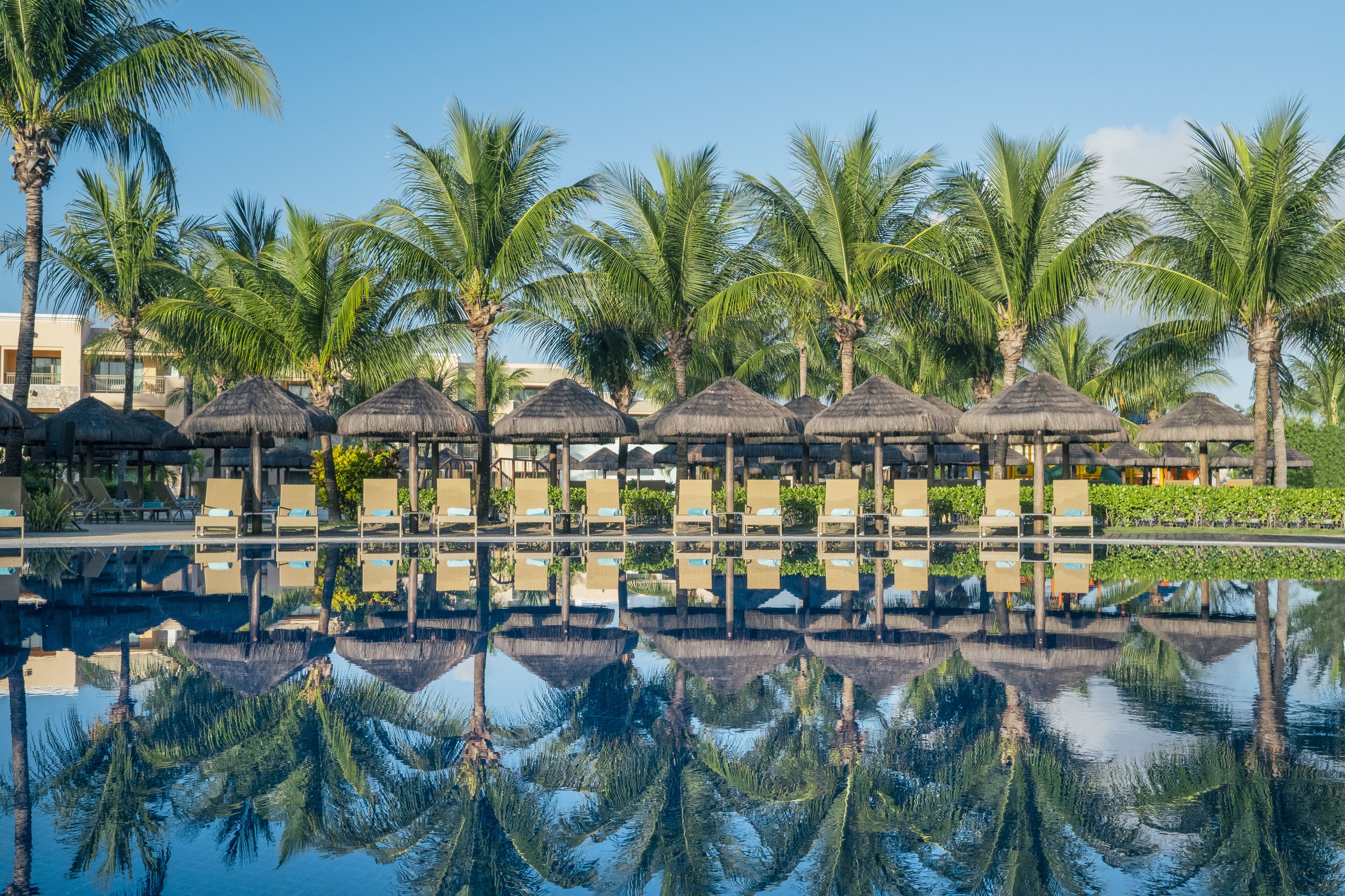 Een resort met een zwembad dat palmbomen en hutten met rieten daken weerspiegelt.