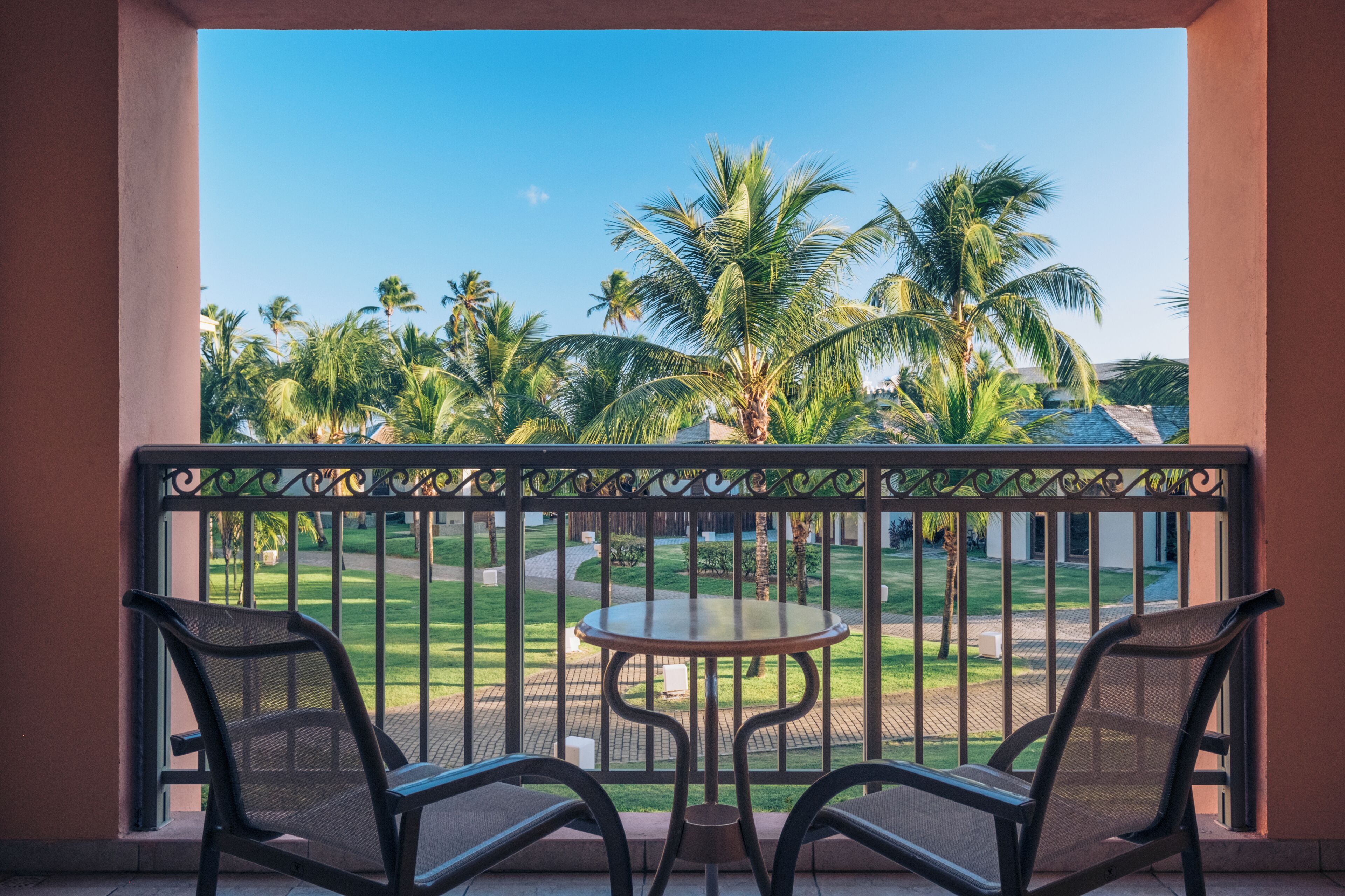 A balcony with two chairs and a small table, overlooking a lawn with palm trees.