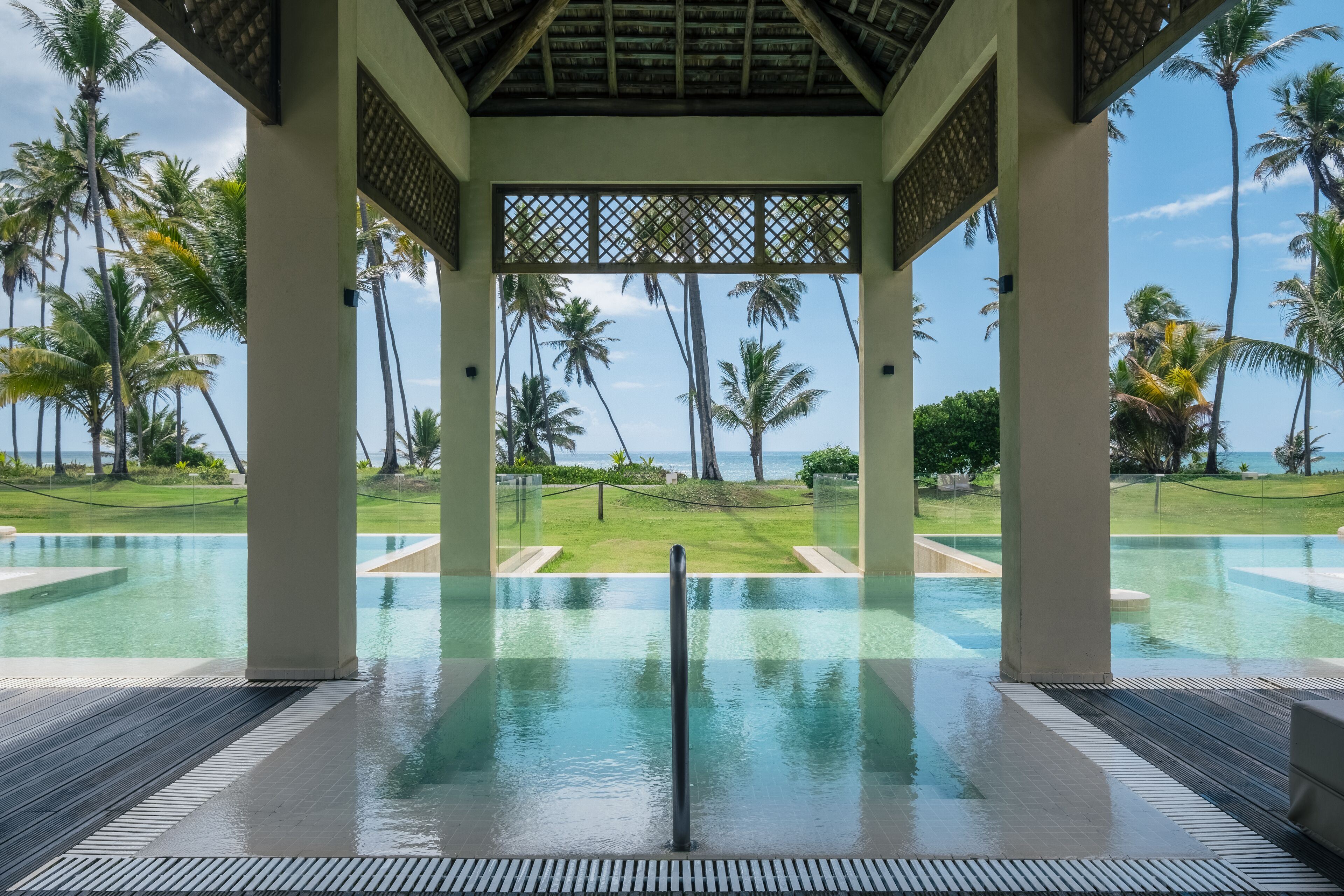 An infinity pool with a clear view of palm trees and a grassy area beyond.