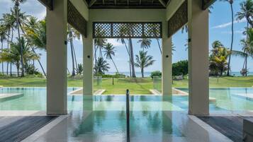 An infinity pool with a clear view of palm trees and a grassy area beyond.