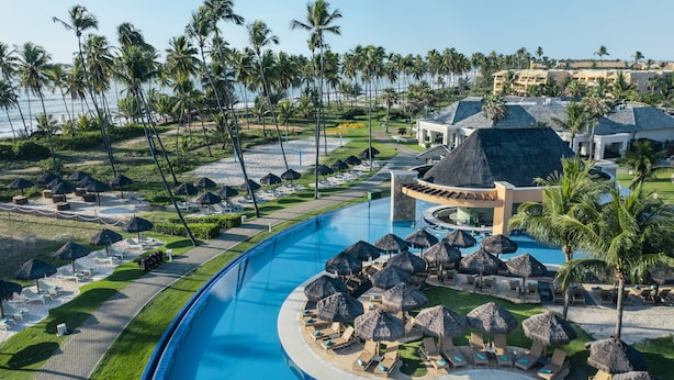 Een resort met een groot zwembad, loungegedeeltes met parasols en palmbomen.