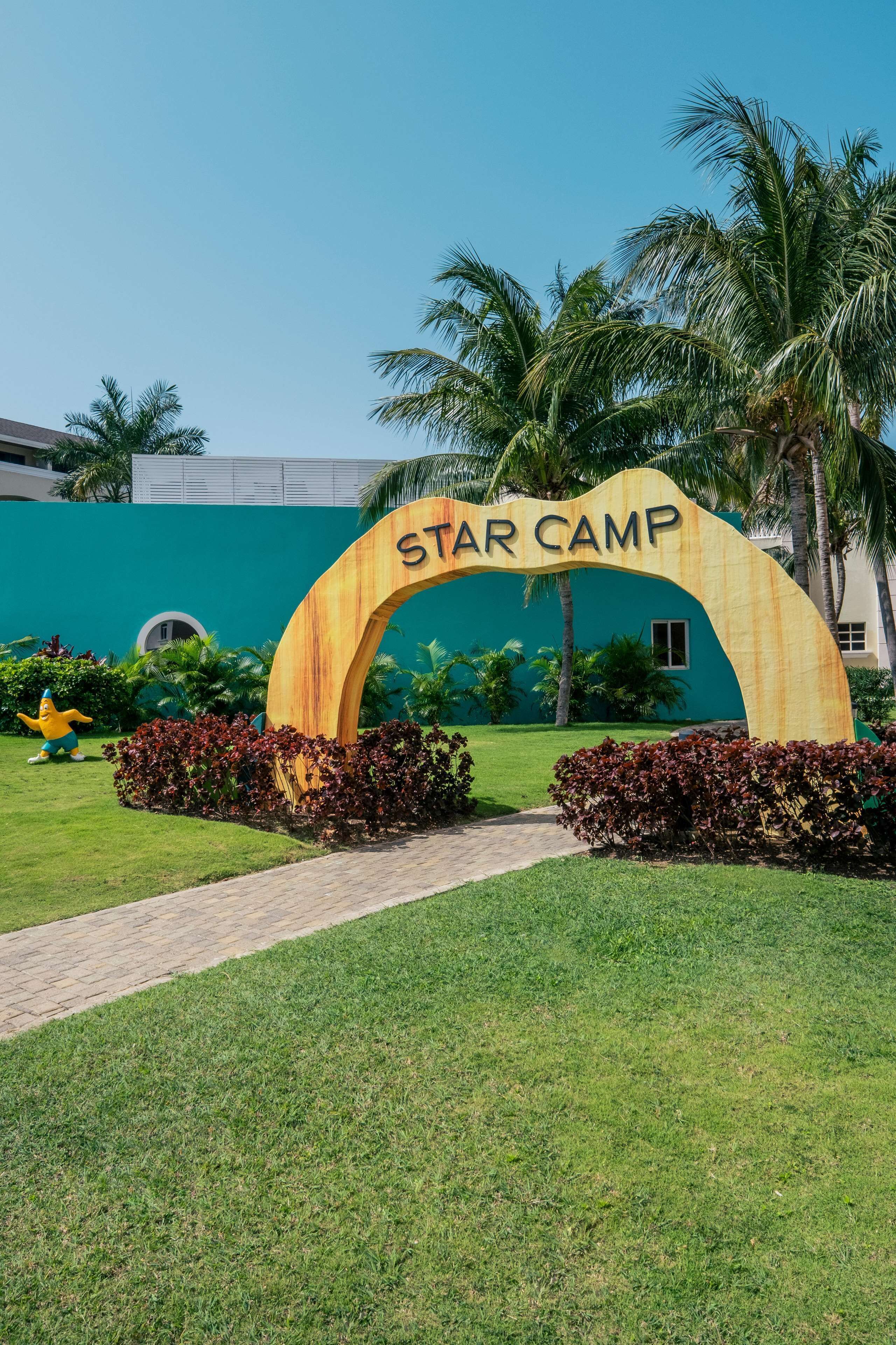 Entree van Star Camp met een grote boog, palmbomen en een verzorgd gazon.