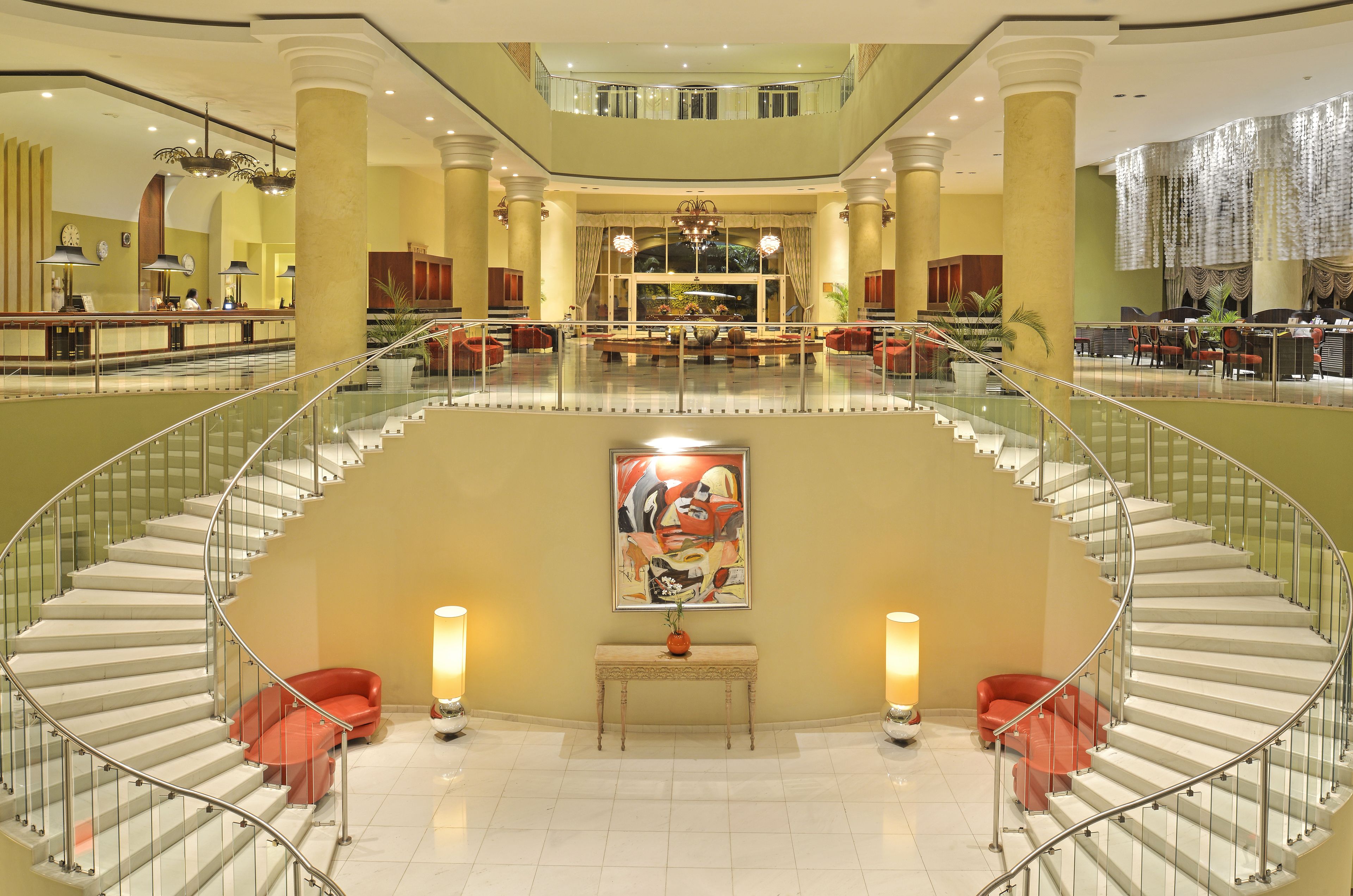 A spacious lobby with a grand staircase, a reception desk, and a large window with a view of the interior.