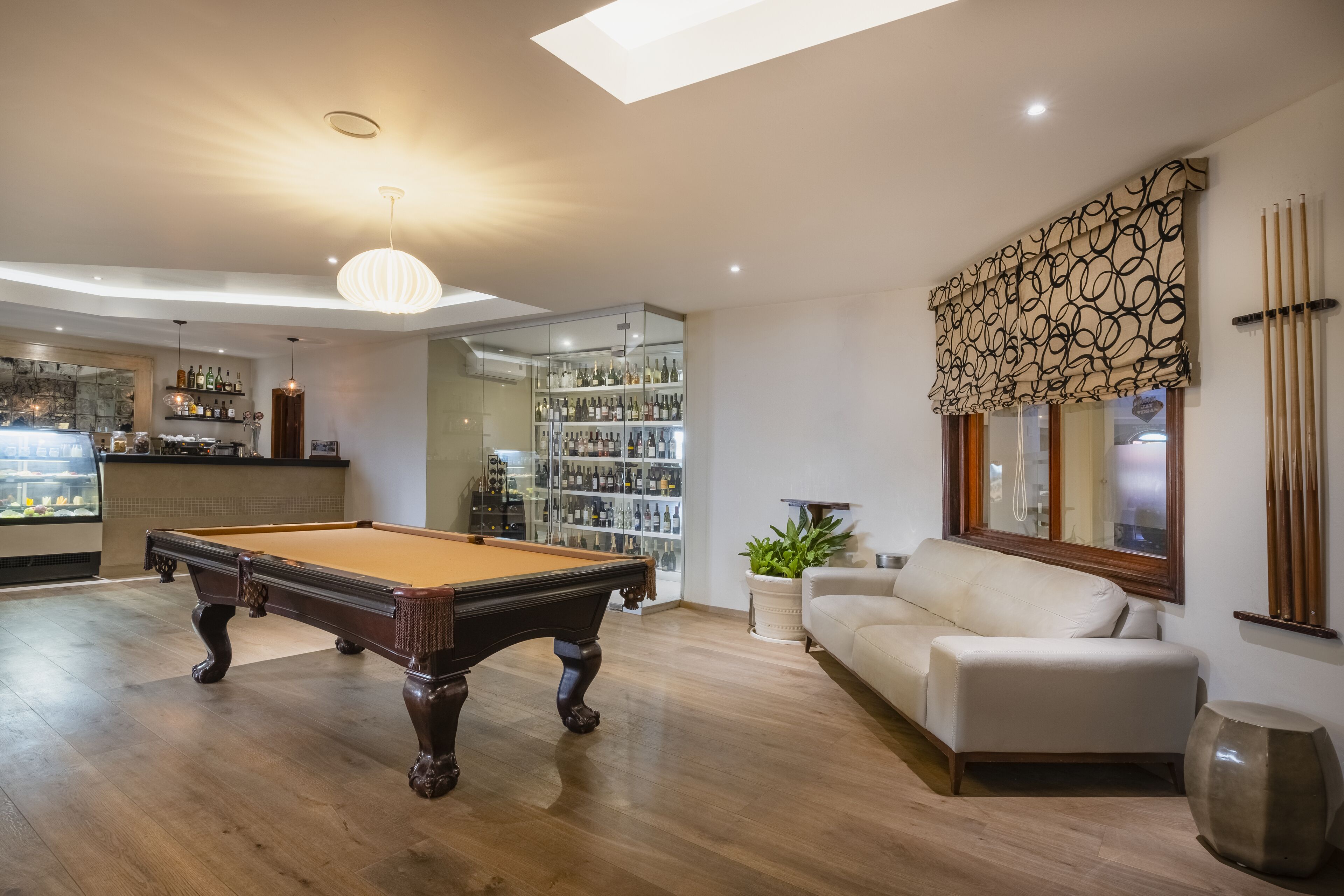 Een biljarttafel in een goed verlichte kamer met een bank en een groot raam met patroonteken gordijnen.