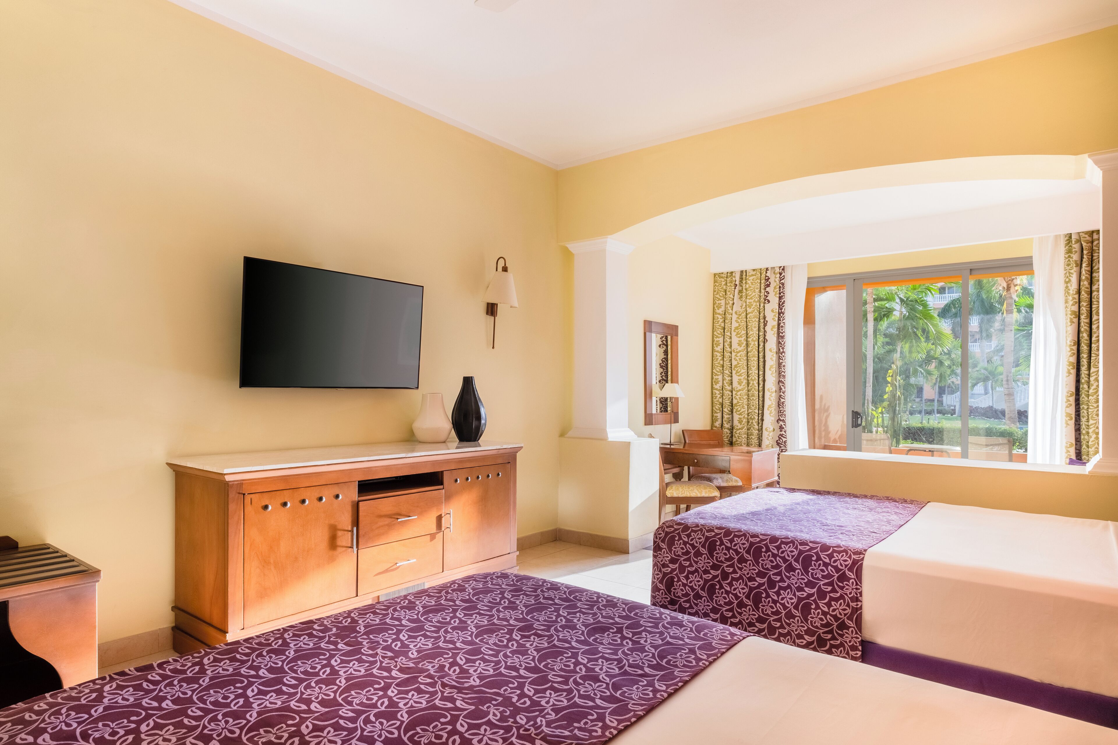 Une chambre d’hôtel avec deux lits, une télévision, une armoire en bois et une fenêtre avec des rideaux.