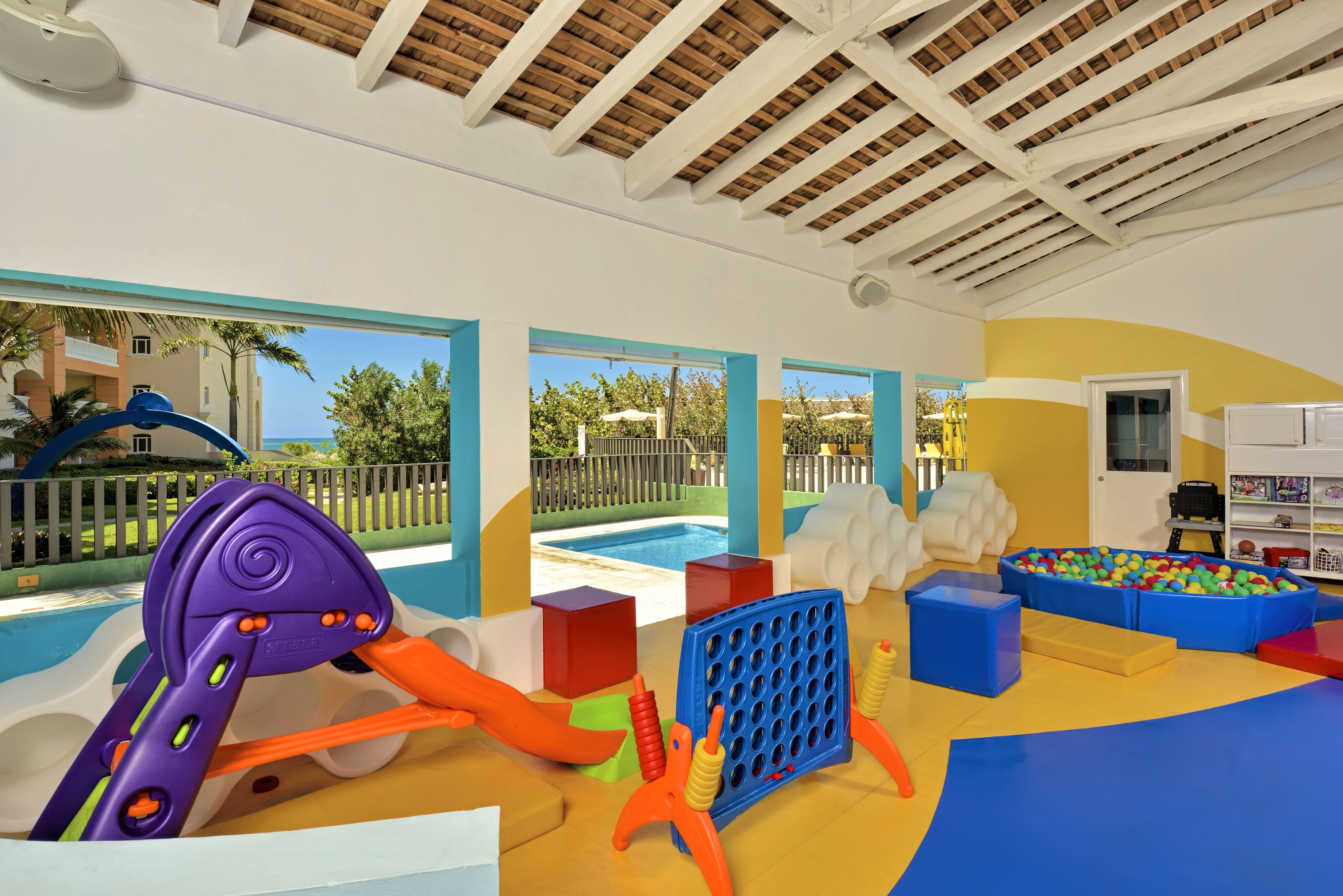 A children's play area with colorful play structures, a pool, and a view of the sea.