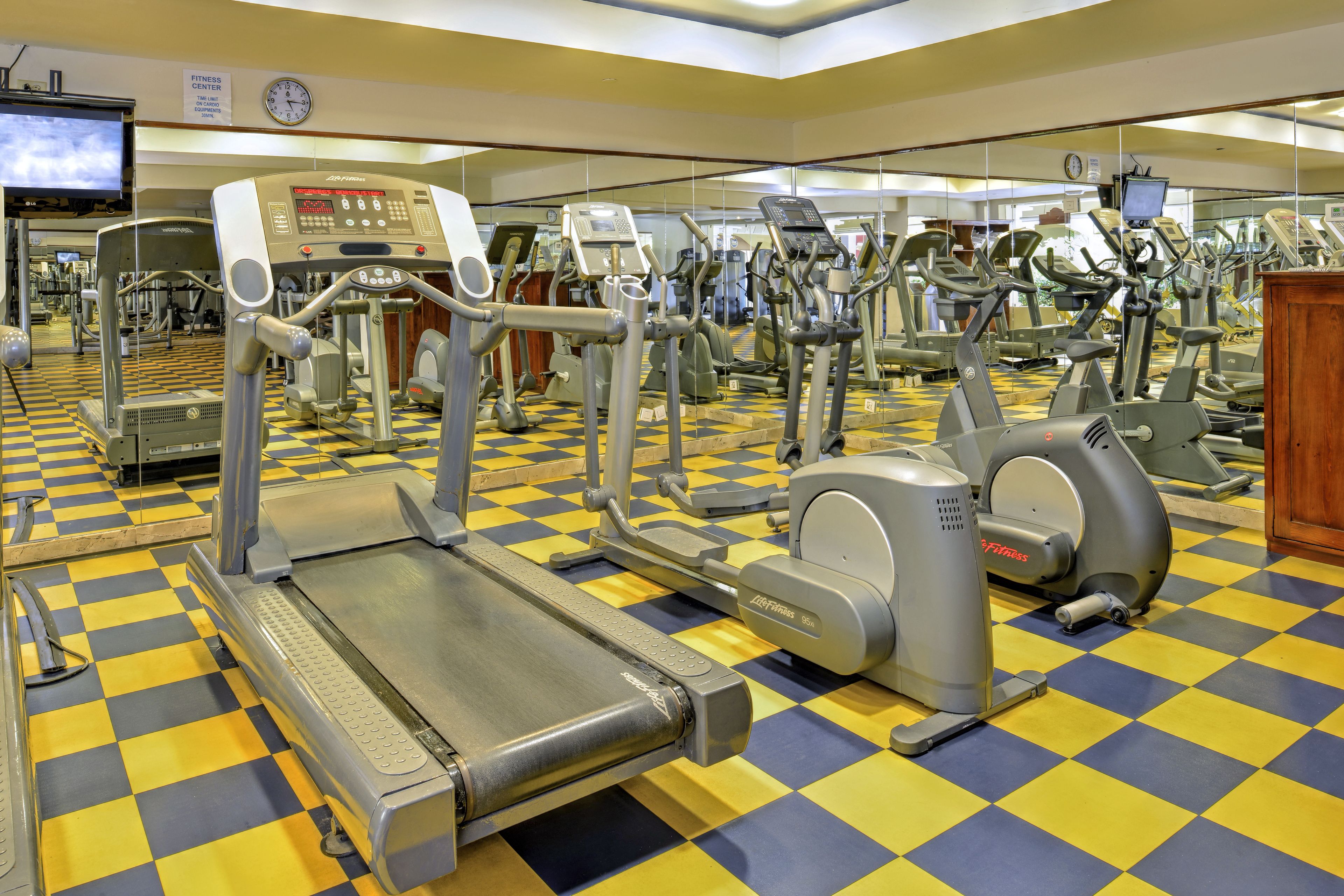 Un gimnasio con diversas máquinas de ejercicio, un reloj y una televisión en la pared.