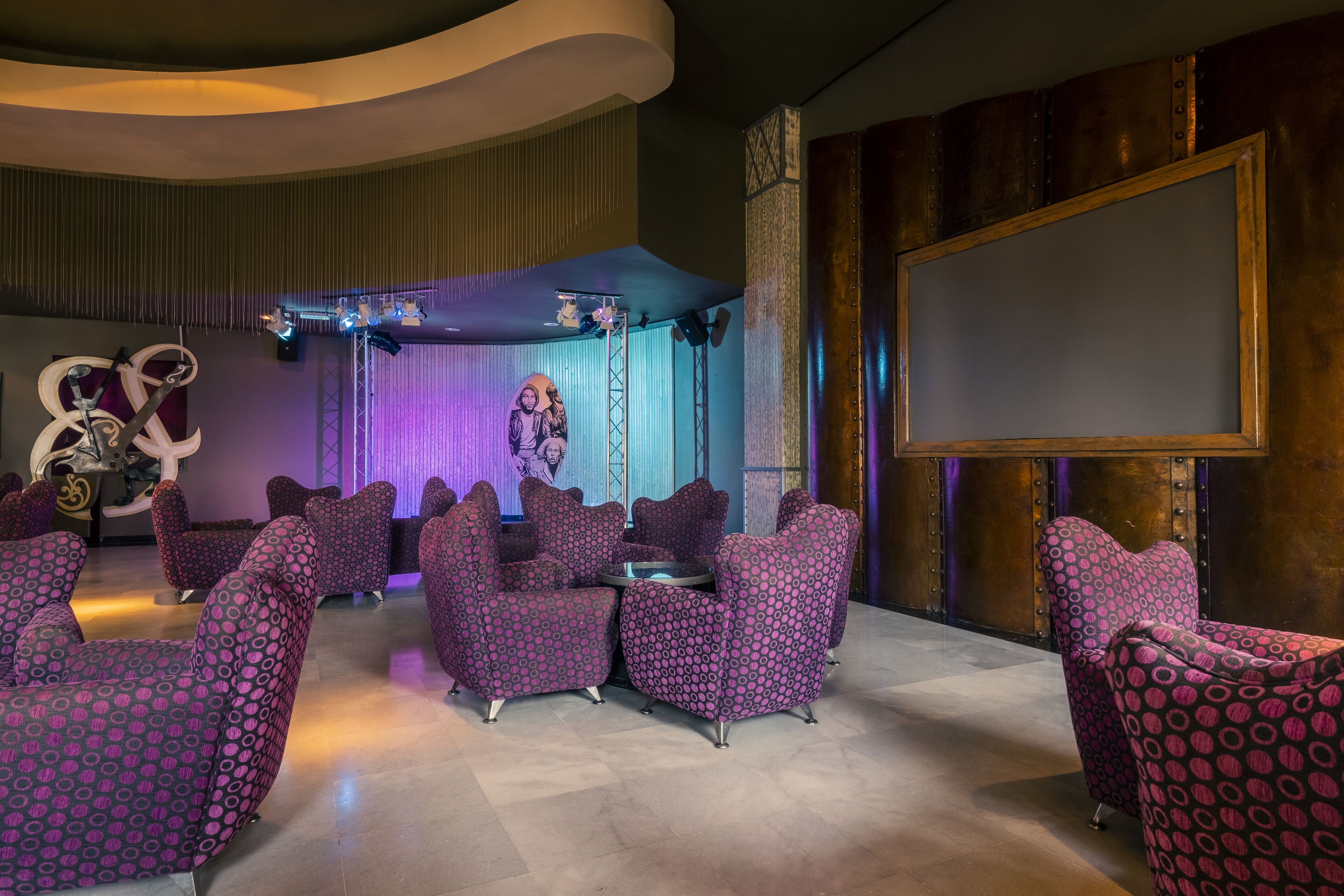 A lounge area with purple patterned chairs and a stage with a large screen.
