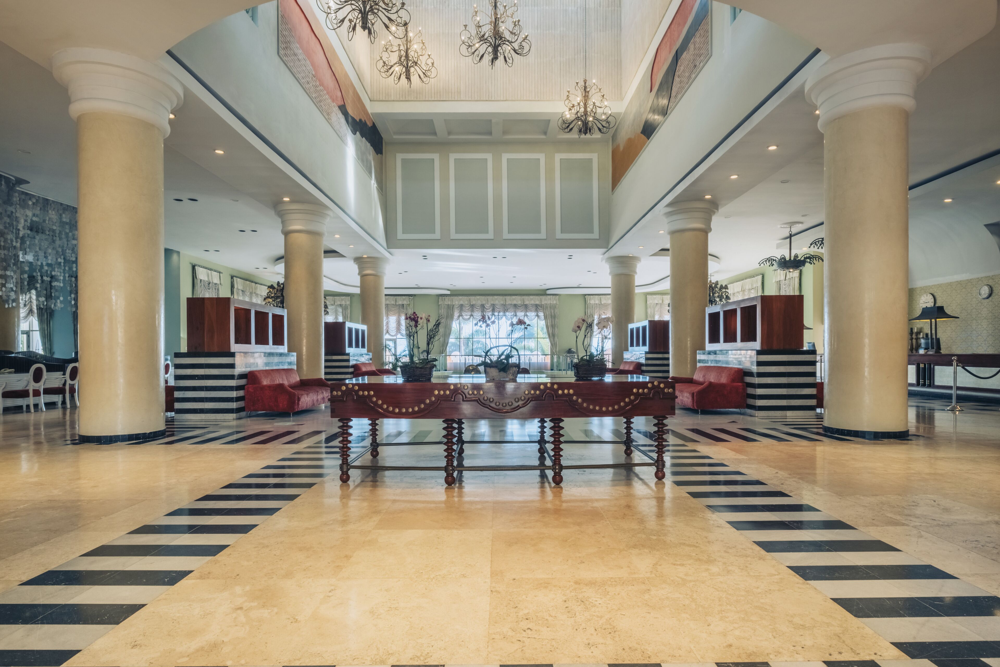 A spacious lobby with a central ornate table, large columns, and a chandelier.