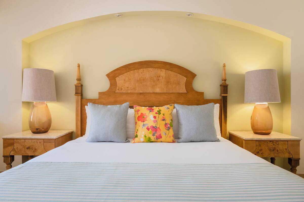 A neatly made bed with a wooden headboard, two bedside lamps, and floral-patterned pillows.