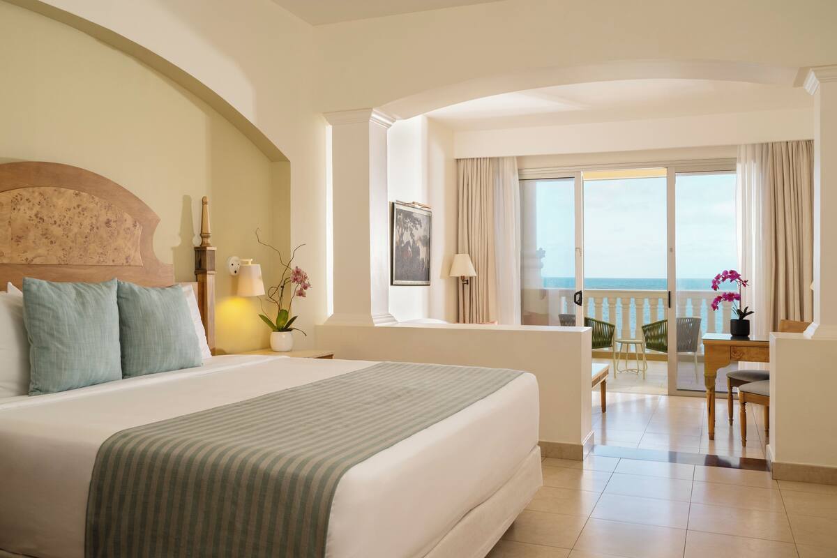 A hotel room with a large bed, a balcony with a view, and a desk with a chair.