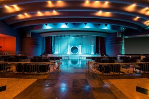 A theater with tiered seating, a stage with curtains, and a large screen.