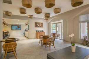 Un interior espacioso y luminoso con una zona de comedor central con mesas y sillas de madera, una cocina equipada con electrodomésticos modernos y un amplio ventanal que proporciona luz natural.