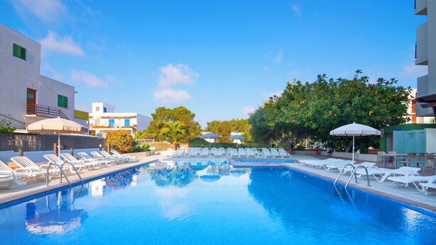 A swimming pool with lounge chairs and umbrellas, surrounded by buildings and trees. - Azuline Hotel S'anfora & Fleming (Sant Antoni de Portmany)